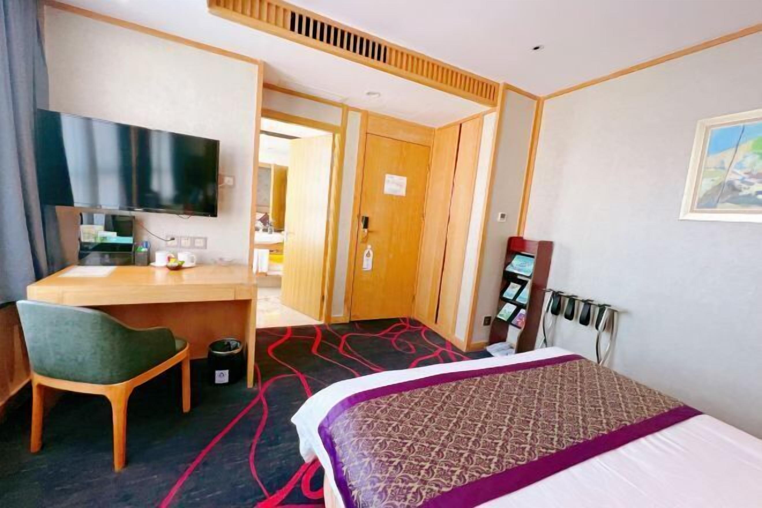 A hotel room with a bed, a desk, a chair, a television, and a door leading to another room.
