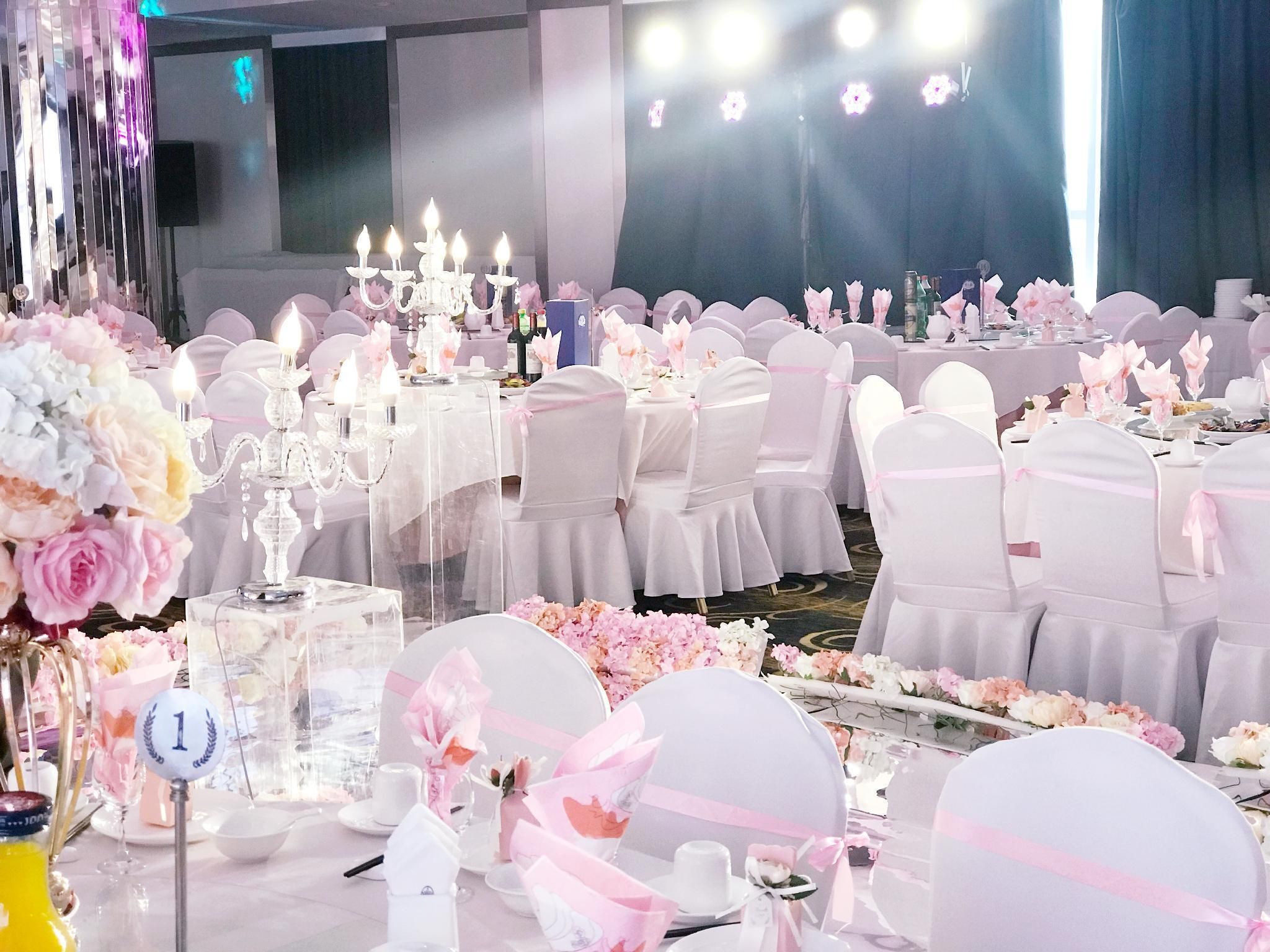 Un salón de banquetes con mesas redondas, sillas blancas y decoración floral.