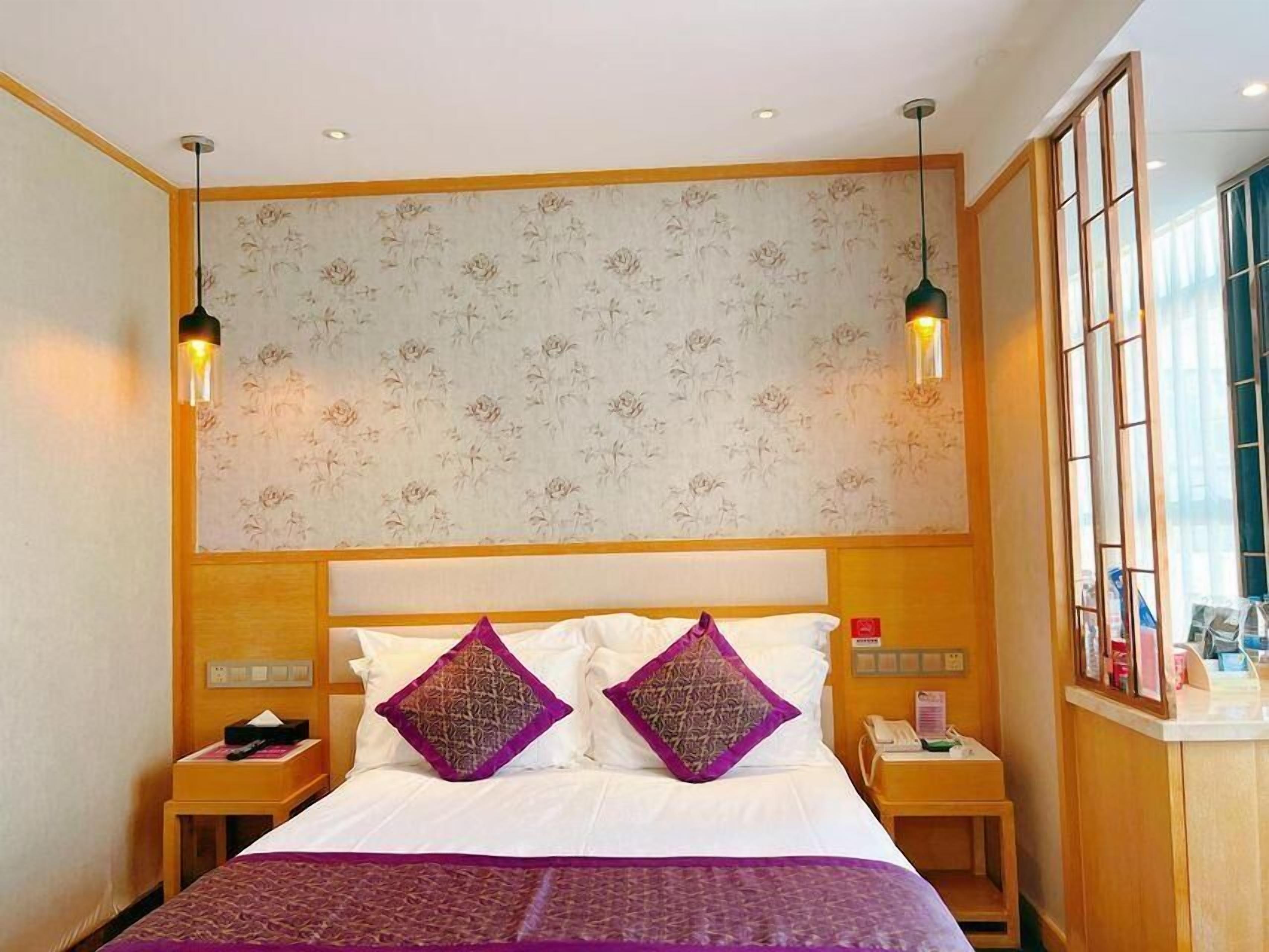Habitación de hotel con una cama grande, dos mesitas de noche, un cabecero de madera, papel tapiz floral y una ventana con vistas.