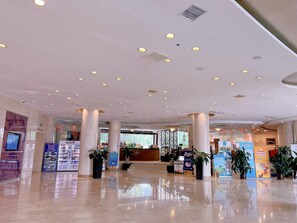 Un vestíbulo espacioso con techo alto, varias columnas y una recepción.