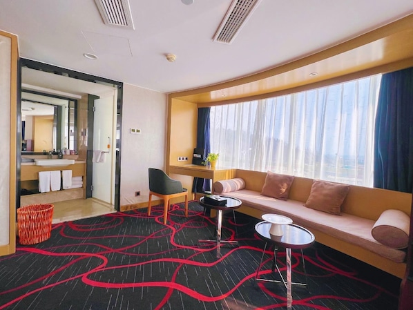 A modern hotel room with a sofa, a small table, a chair, and a large window with curtains. - Sophia International Hotel (Qingdao)