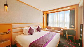 A hotel room with a large bed, a desk, a chair, and a window with curtains.