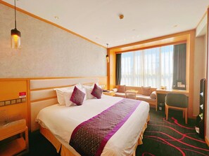 Una habitación de hotel con una cama grande, un escritorio, una silla y una ventana con cortinas.