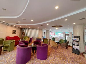 A lobby with purple and green chairs, a reception desk, and a patterned carpet. - Sophia International Hotel (Qingdao)