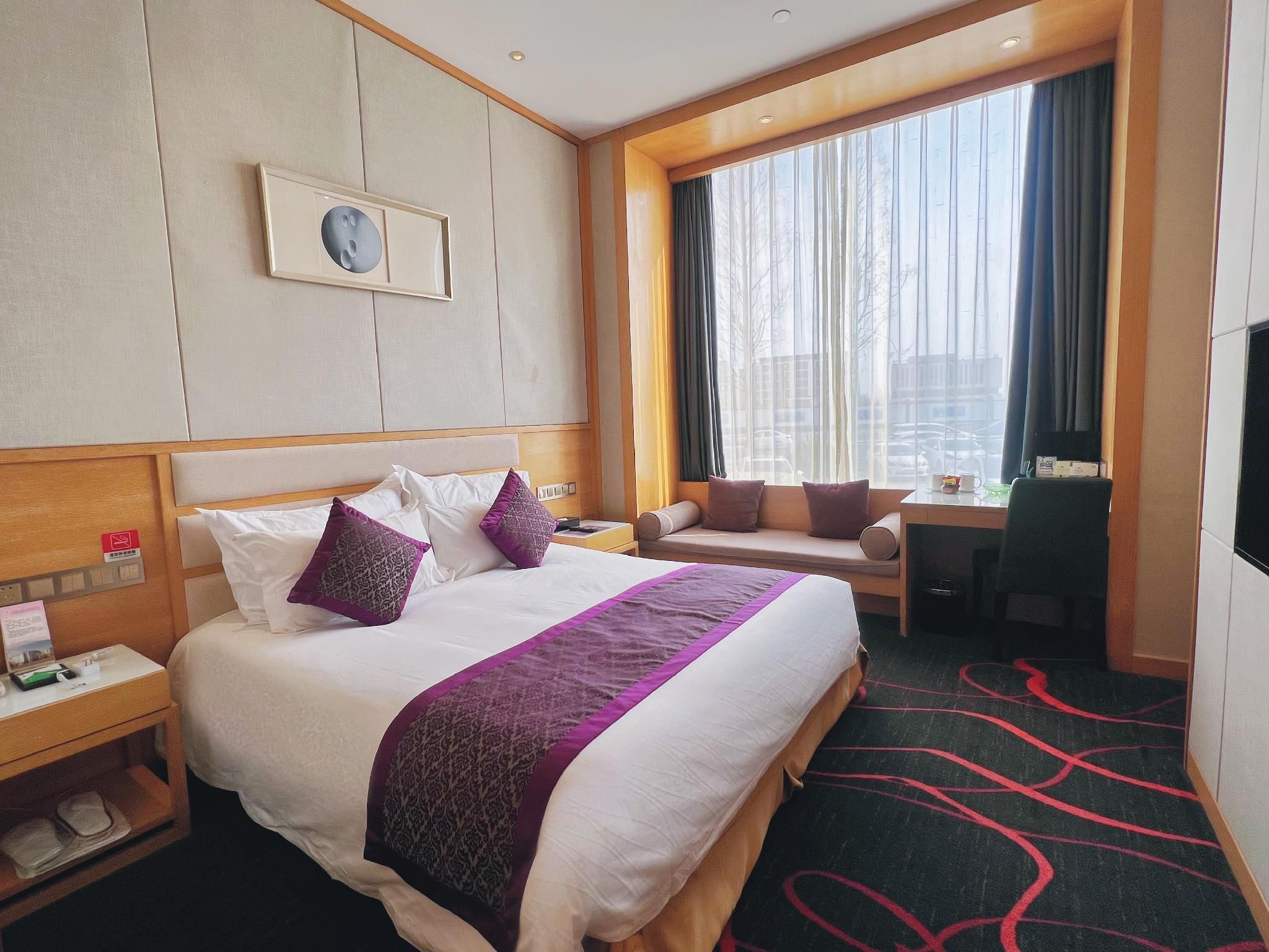 A hotel room with a large bed, a desk, a chair, and a TV.