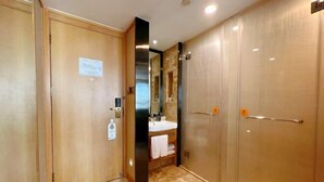 Un baño de hotel con puerta de madera, espejo, lavabo y zona de ducha.
