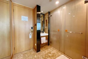 A hotel bathroom with a wooden door, a mirror, a sink, and a shower area. - Sophia International Hotel (Qingdao)