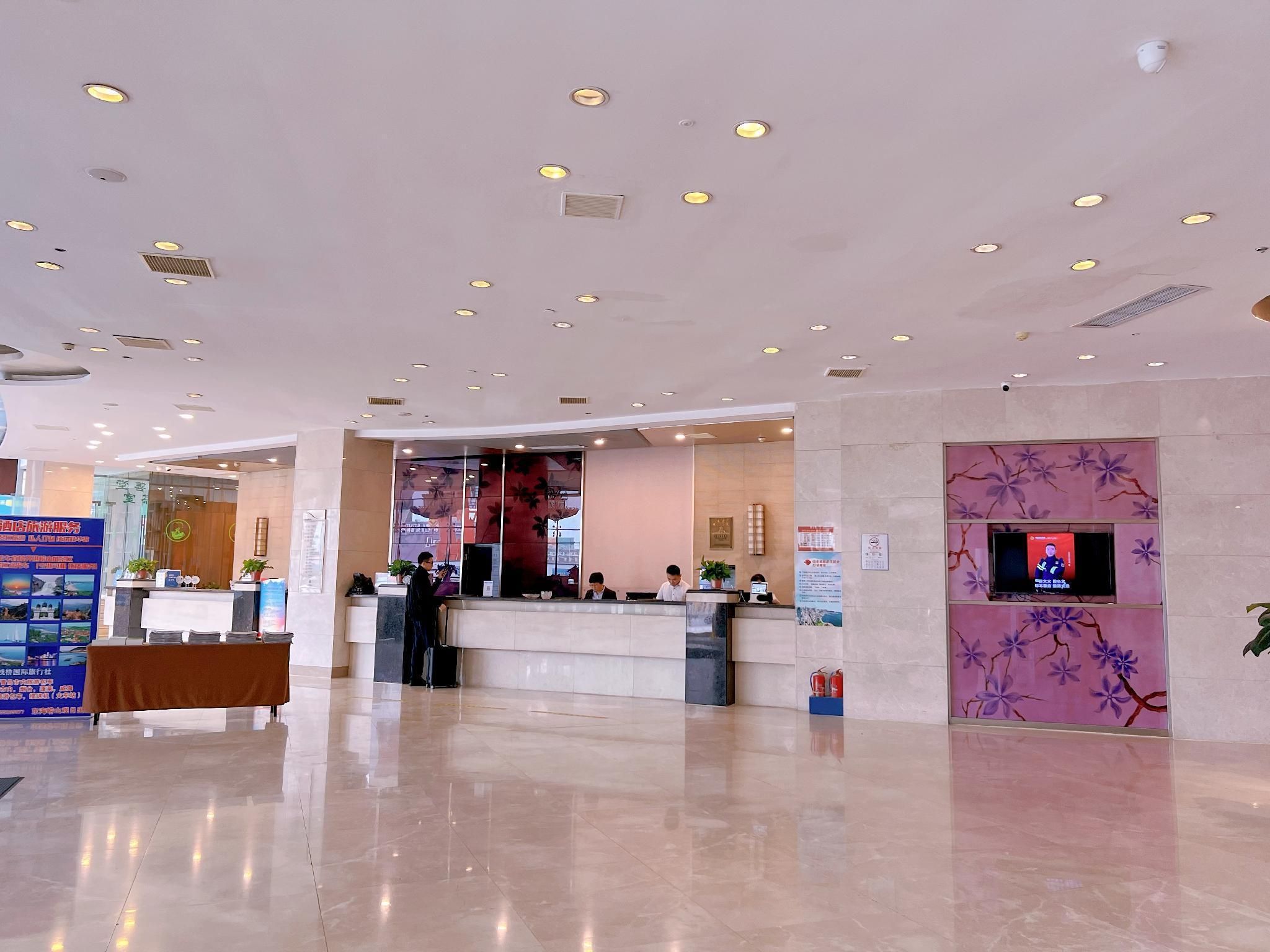 Un vestíbulo de hotel con una recepción, una pantalla digital y un cartel grande.