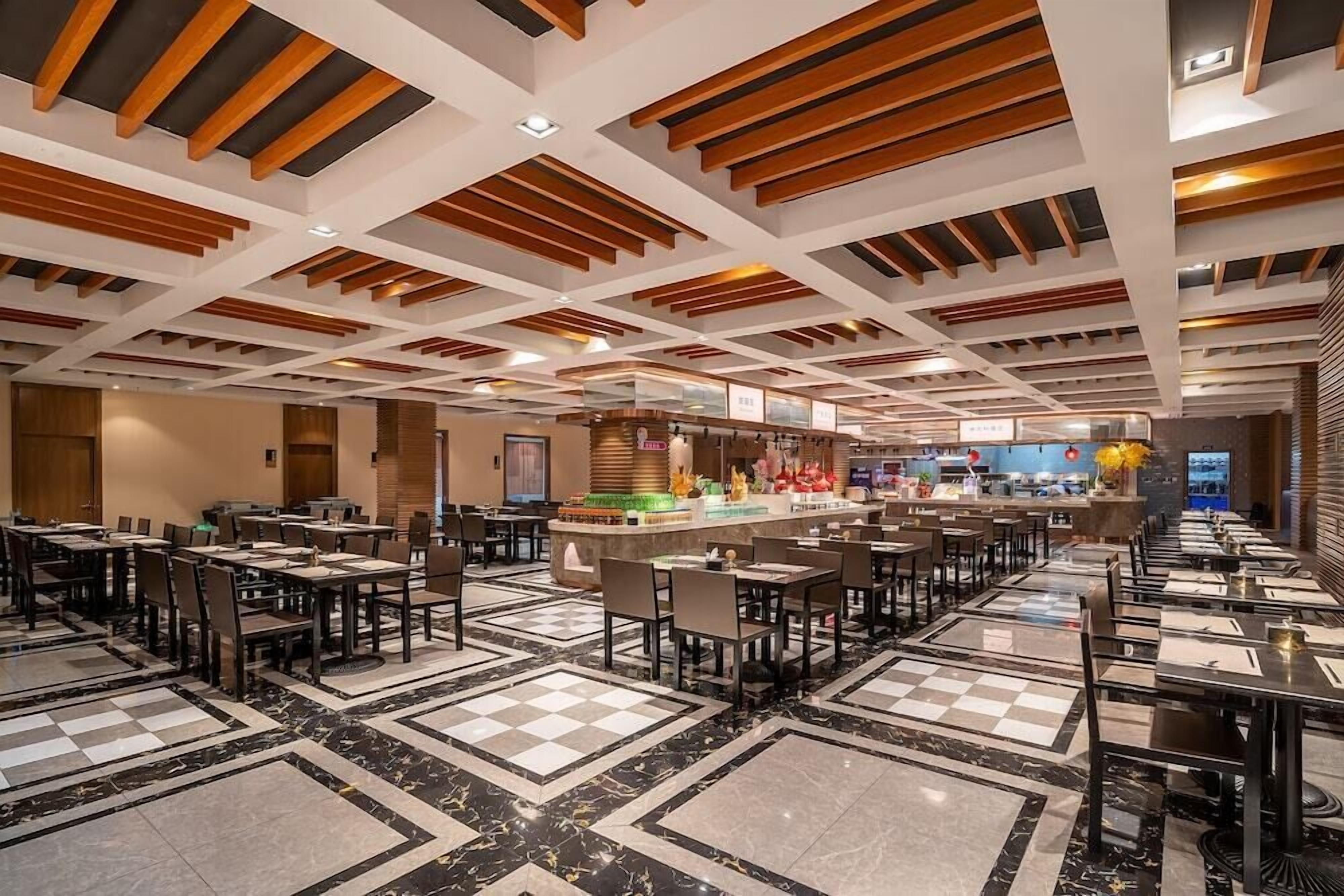 A spacious hotel lobby with a checkered marble floor, wooden ceiling beams, and a central bar area.