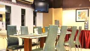 A dining area with a long table and multiple chairs, a television mounted on the wall, and a water dispenser. - ZEN Rooms KH Mas Mansyur (Surabaya)