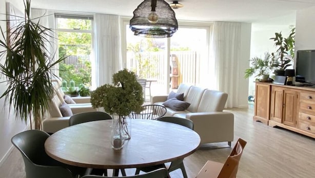 A modern dining area with a round table, green chairs, and a hanging pendant light. - Ferienhaus in die Rue Royale (Middelburg)