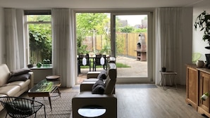 A modern living room with a sofa, coffee table, and a view of the backyard through large sliding doors. - Ferienhaus in die Rue Royale (Middelburg)