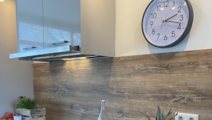 A modern kitchen with a wooden countertop, a built-in stove, a clock on the wall, and a fruit basket. - Ferienhaus in die Rue Royale (Middelburg)
