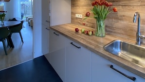 A modern kitchen with white cabinets, a wooden countertop, and a stainless steel sink. There is a vase with tulips and apples on the counter. - Ferienhaus in die Rue Royale (Middelburg)