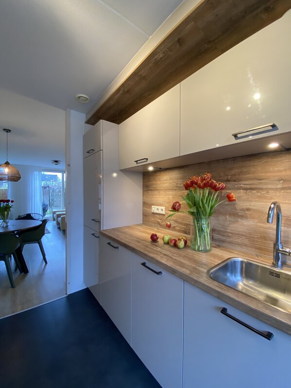 A modern kitchen with white cabinets, a wooden countertop, and a stainless steel sink. There is a vase with tulips and apples on the counter.