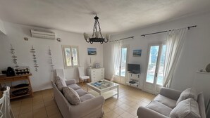 A spacious living room with a sofa, a coffee table, a TV, and a view of the outdoors. - Four bedroom villa with private pool with stunning views and beautiful sunsets (Halikeri)