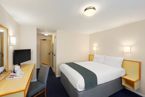 Quarto de hotel com cama, escrivaninha com cadeira, televisão e espelho.
