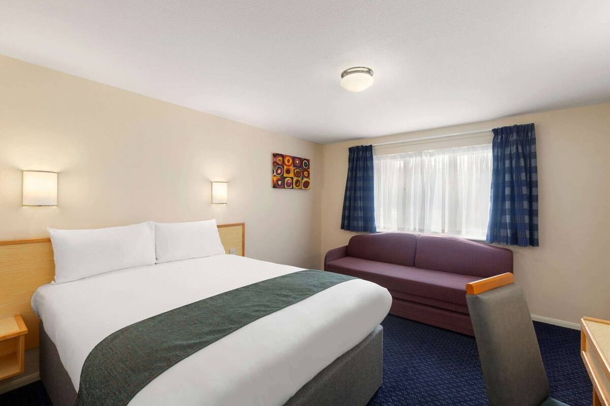A hotel room with a bed, a sofa, a small table, and a window with curtains.