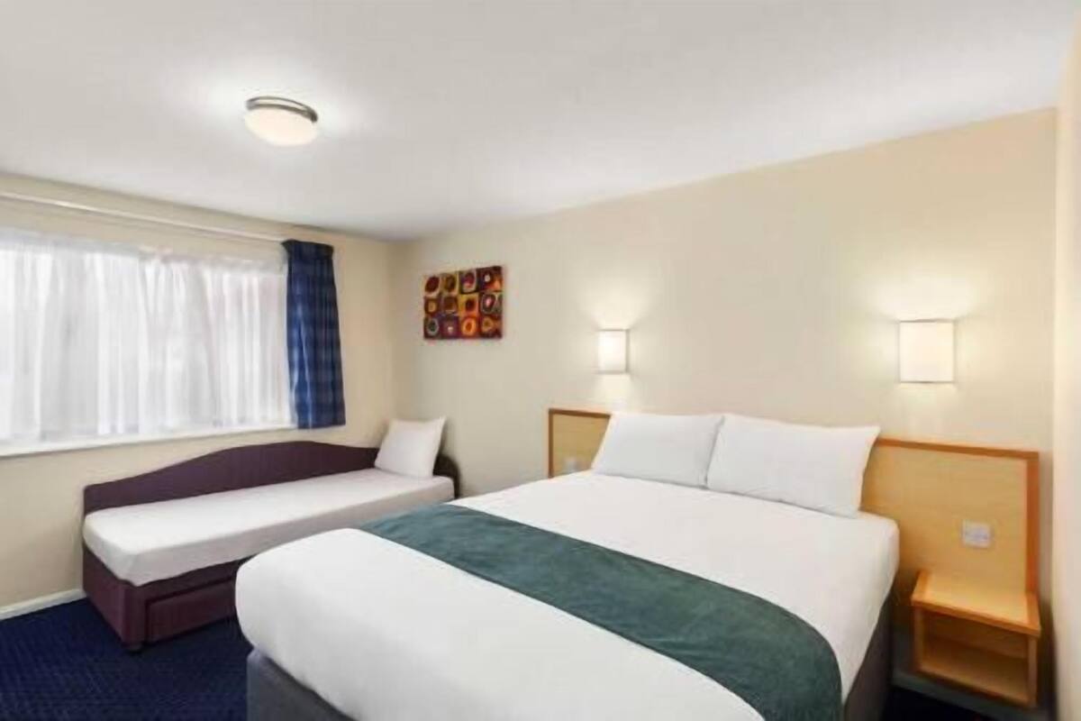A hotel room with a bed, a sofa, a window with curtains, and wall-mounted lights.