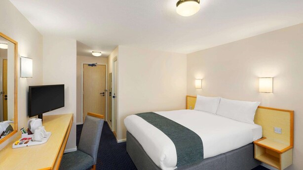 A hotel room with a bed, a desk with a chair, a television, and a mirror. - Days Inn by Wyndham Sutton Scotney South (Winchester)