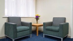 A corner room with two grey armchairs, a small wooden table, and a vase of flowers. - Days Inn by Wyndham Sutton Scotney South (Winchester)