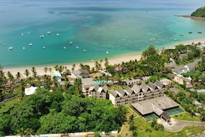 Un resort con varias edificaciones, una playa y barcos en el agua.