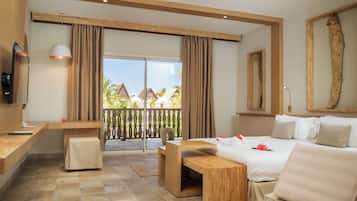 A hotel room with a bed, a desk, a TV, a balcony with a view of palm trees and buildings.
