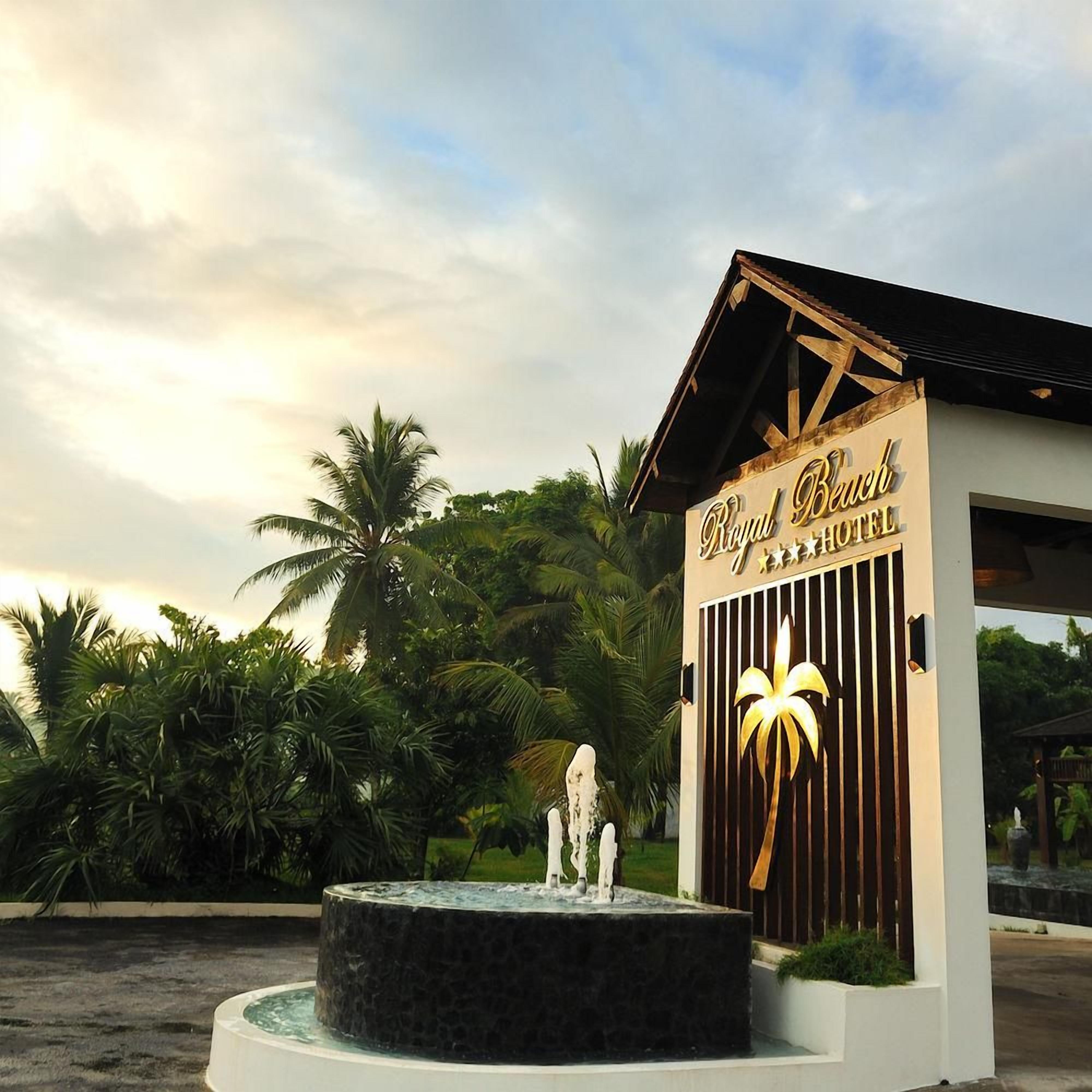 A hotel entrance with a sign reading 'Royal Beach Hotel' and a palm tree sculpture.