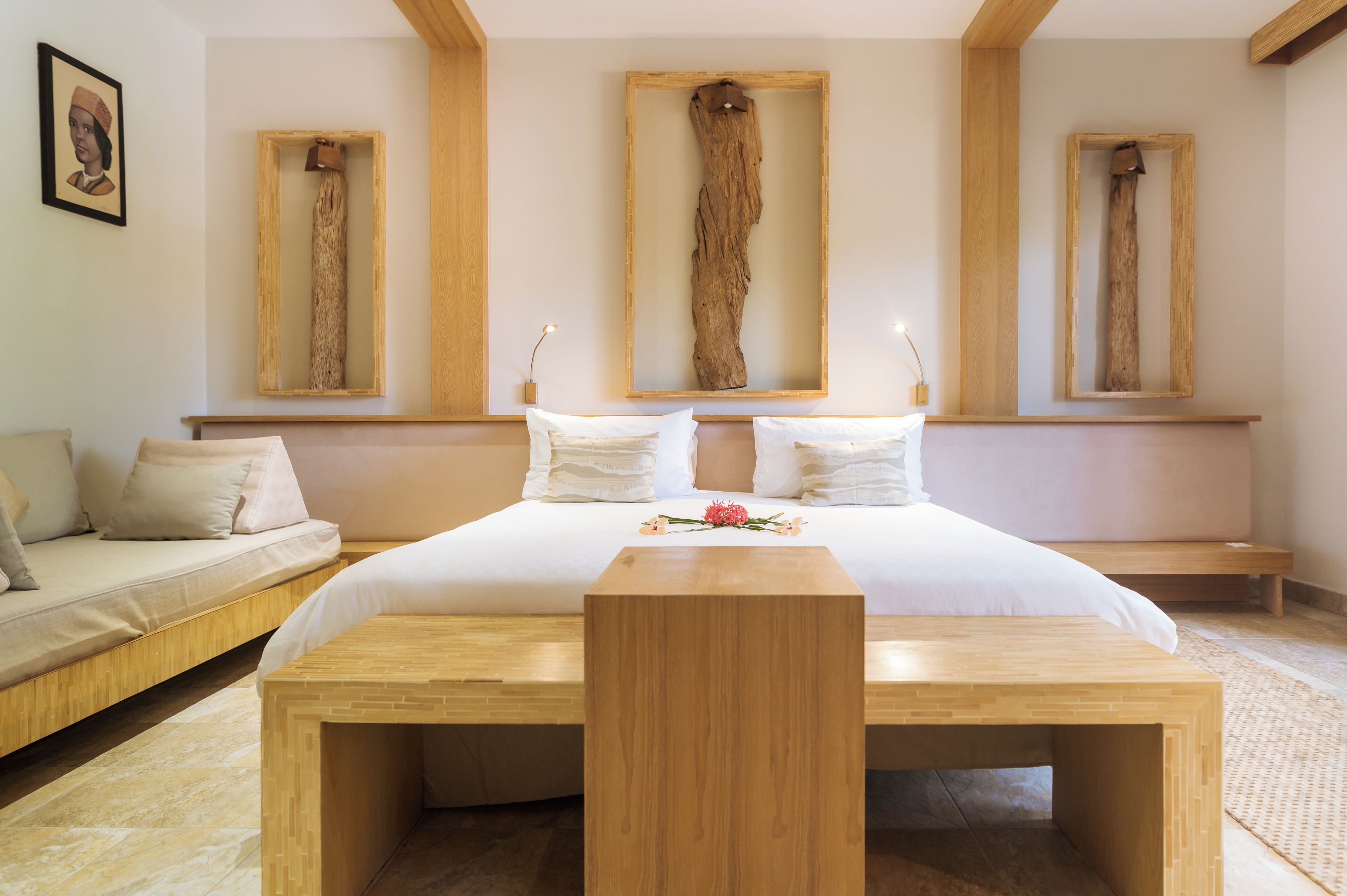 A bedroom with a large bed, a wooden bench, and three wooden frames on the wall.