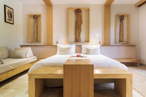 A bedroom with a large bed, a wooden bench, and three wooden frames on the wall.