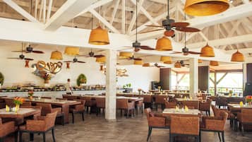 A spacious restaurant with high ceilings, wicker furniture, and pendant lighting.
