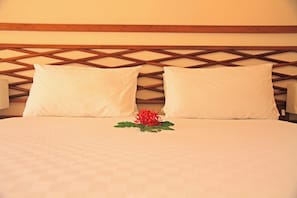 Cama com colcha branca, duas almofadas brancas e um arranjo de flores vermelhas.