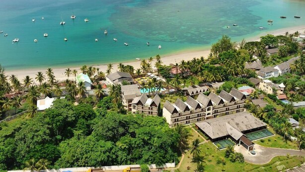 Un resort con varias edificaciones, una playa y barcos en el agua.