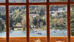 Una habitación con un ventanal grande que da a un lago con barcos, rodeada de árboles y edificios.