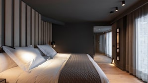 Quarto de hotel moderno com uma cama grande, uma mesa de cabeceira e um criado-mudo. O quarto tem piso de madeira e uma janela grande com cortinas.
