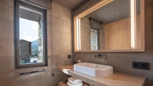 Uma casa de banho moderna com uma janela ampla, uma banheira independente e uma toucador de madeira.