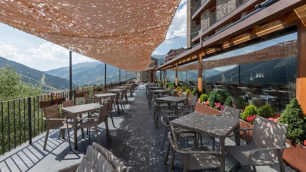 Terraço ao ar livre com mesas e cadeiras, varanda de madeira e vista para montanhas.