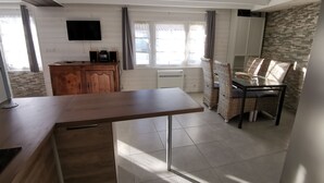 Un'ampia cucina con un tavolo di legno, sedie in vimini, un mobiletto a incasso e un televisore montato a parete.