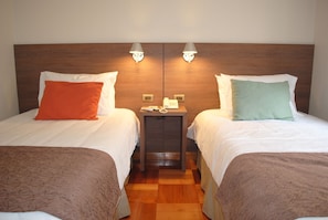 Two single beds with white linens and decorative pillows, flanked by wall-mounted lamps and a wooden nightstand.