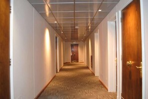 Leading to a door at the end, this corridor features a wooden floor and white walls.
