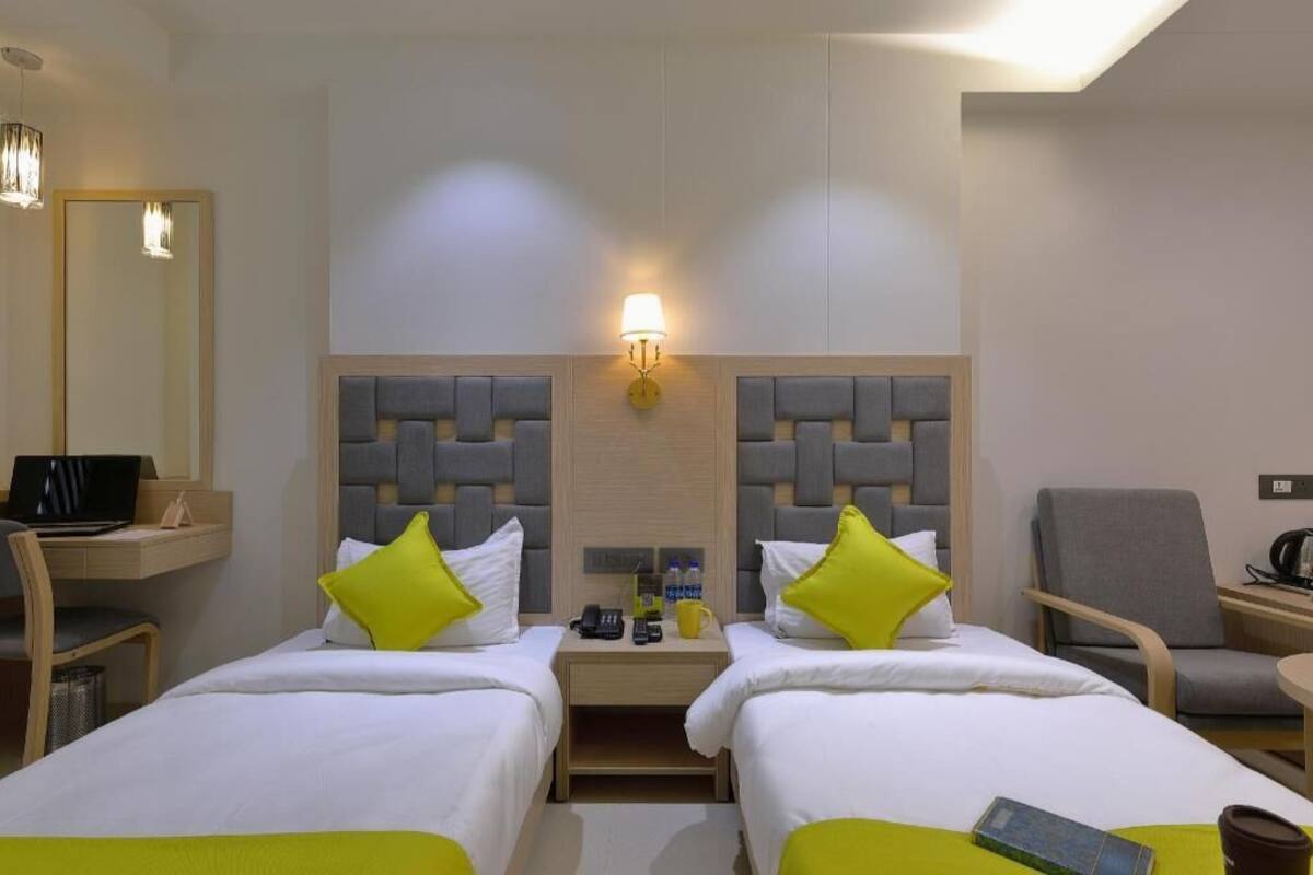 A hotel room with two beds, a desk, a chair, a lamp, and a mirror.