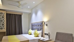 A hotel room with a bed, a chair, a small table, and a ceiling fan. - Hotel Sifat International (Surat)