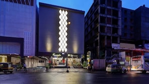 A building with a prominent diamond-patterned light installation on its facade, a storefront with signage, and a parked vehicle in front. - Hotel Sifat International (Surat)