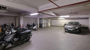 A parking garage with multiple motorcycles and a car parked. - Hotel Sifat International (Surat)
