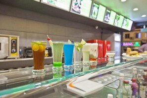 A bar area with various colorful drinks and a menu board in the background.