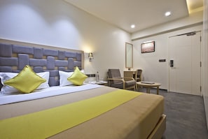 A hotel room with a large bed, two armchairs, a small table, and a door.