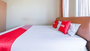 Ein Hotelzimmer mit einem ordentlich bezogenen Bett, einer roten und weißen Tagesdecke sowie zwei Kissen mit der Aufschrift 'YOYO'.