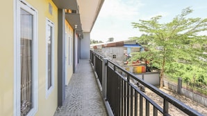 Ein schmaler Balkon mit Fliesenboden, begrenzt von einem schwarzen Geländer, mit Blick auf ein Wohngebiet mit Bäumen und Gebäuden.