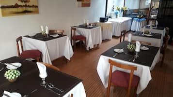 Restaurante com várias mesas preparadas para refeições, com toalhas de mesa brancas e cadeiras de madeira.