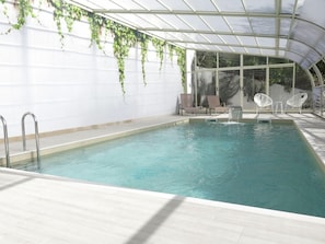 Una piscina interior con agua cristalina, rodeada de paredes blancas y un techo de cristal.